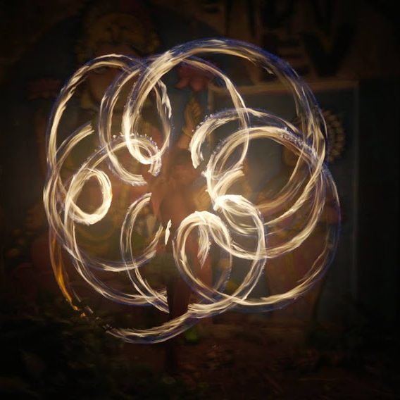 Fotografía de larga exposición donde se aprecia la geometría de una flor de la vida pintada con fuego. Maka dibuja patrones sagrados bailando con sus cariocas de fuego