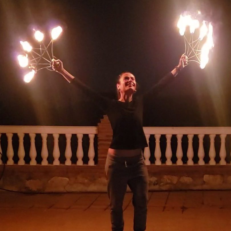 Cristina, estudiante de Maka, en una clase de baile con fuego, bailando con los abanicos de fuego encendidos. Su cara es de felicidad