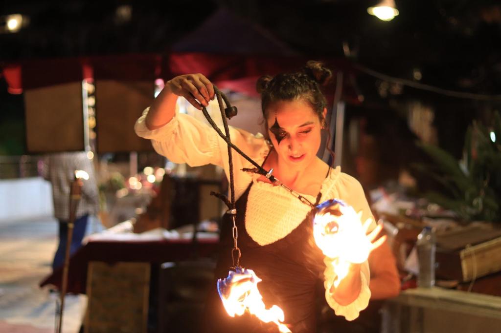 Espectáculo de fuego en feria medieval en Almuñécar, Granada. Maka, con un atuendo de arlequín, acaricia el fuego de sus cariocas